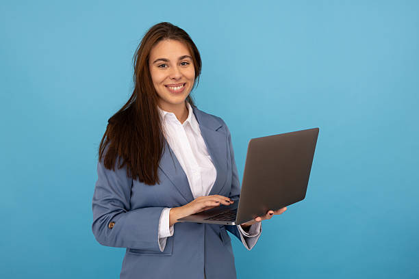 istock Professional businesswoman working on laptop, smiling confidently against blue studio backdrop 2219704016