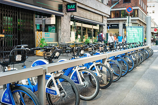 Pedestrians walk past a bike share station in downtown Oslo, Norway on a sunny day.