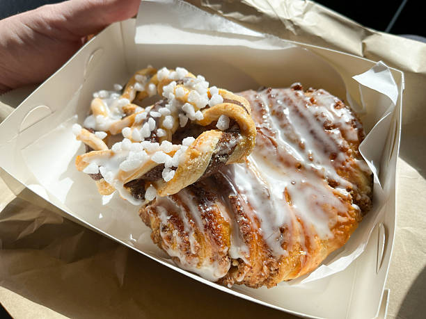 A white pastry box holds a hazelnut Danish with icing sugar and a chocolate twist topped with rock sugar
