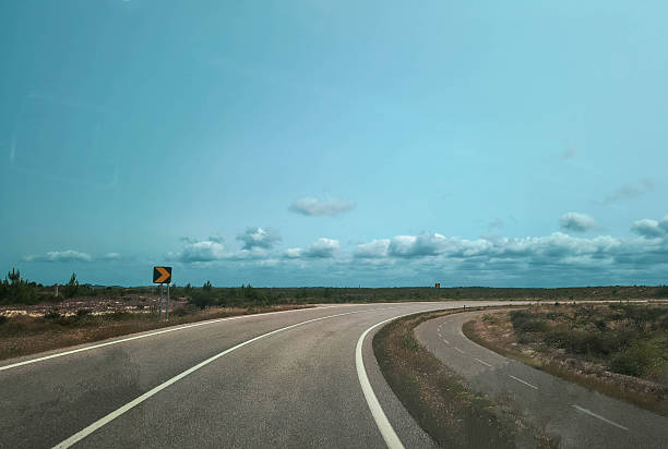 istock Open road view with leading lines. Curves ahead under a bright, cloudy sky. Evokes travel, adventure, and freedom. Ideal for transportation, tourism, or personal journey. 2219706944