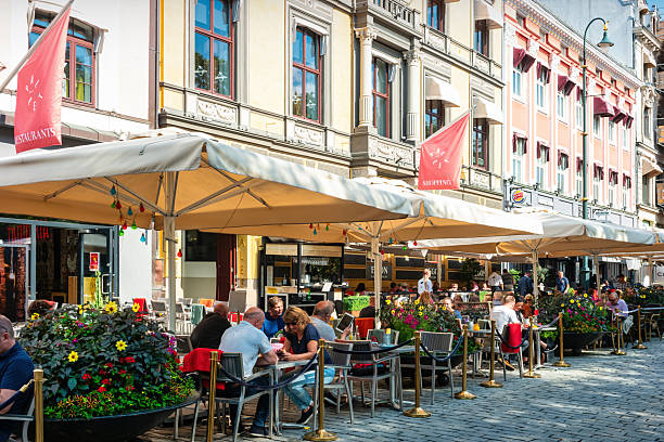 People sit on a restaurant patio at Paleet arcade in downtown Oslo, Norway on a sunny day.