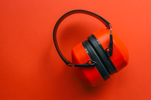 Red and black protective ear muffs for hearing protection placed on solid orange background, isolated studio shot with copy space.