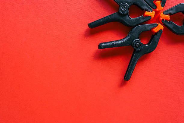Four black plastic spring clamps with orange tips arranged diagonally on bright red background. Minimalistic tool concept with strong contrast and copy space.