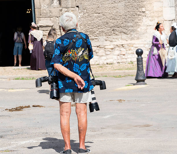 Arles, France - June 30, 2024: Tourist with cameras hanging from his shoulders wait for women to exit the church at the Fete du Costume festival where over 500 women dress in traditional attire from their region depicting differing lace and hats in this annual June festival, Arles, France, Europe