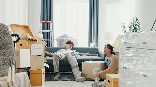 young asian couple sit on sofa couch take a rest from organize moving carton box full of messy stuff in living room at new house. husband and wife move new house, apartment rent and ownership. - cuộc nói chuyện cặp đôi tức giận hình ảnh sẵn có, bức ảnh & hình ảnh trả phí bản quyền một lần
