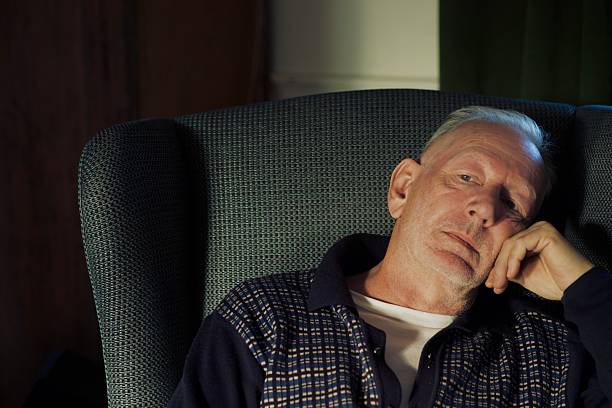 A man comfortably sits in an armchair, looking up and thinking about the past