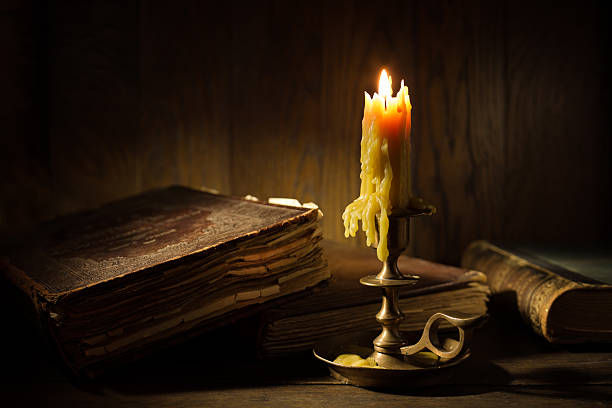 istock Antique bronze candlestick burning in dark room with old books. 2219731737