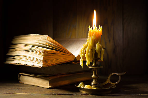 istock Ancient bronze candlestick burning near antique books. Medieval still life 2219731791