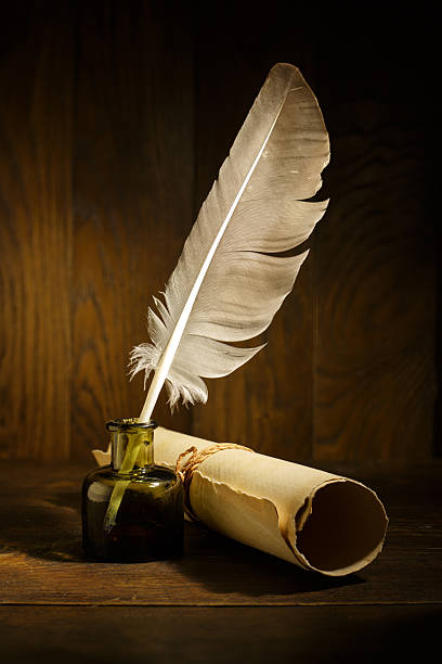 istock Ancient paper scroll with quill pen on old wooden table. Feather for calligraphy, old education, vintage fonts. 2219731796