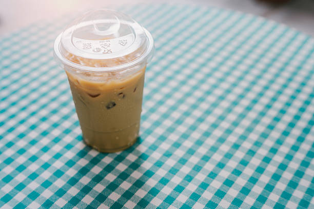 Drink in cafe. Iced coffee in a clear cup on a checkered tablecloth, showcasing a refreshing summer beverage for warm days and outdoor relaxation.