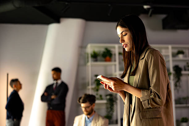 istock Focused businesswoman using smartphone in modern office with colleagues in background 2219737131