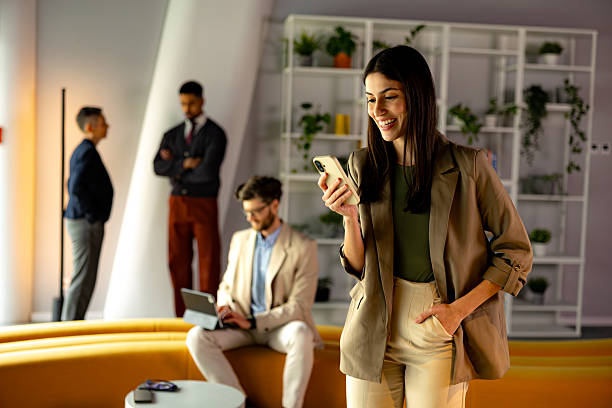 istock Young businesswoman using smartphone in modern office with colleagues working in background 2219737150