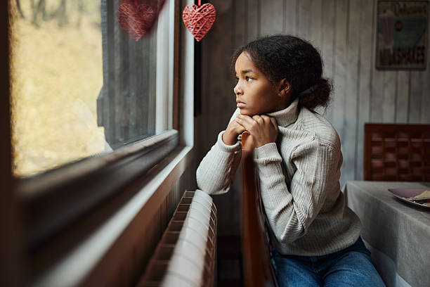 Sad African American girl day dreaming while looking through window from home.