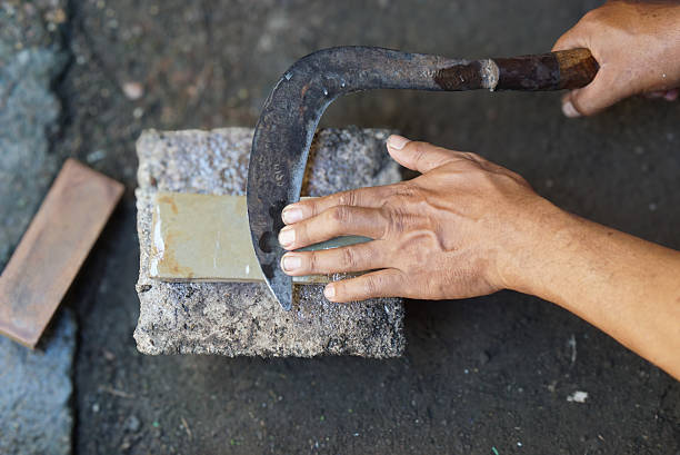 The blacksmith is sharpening the sickle with a traditional whetstone.
