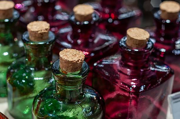 A collection of decorative glass bottles in shades of green and red, each topped with a cork.