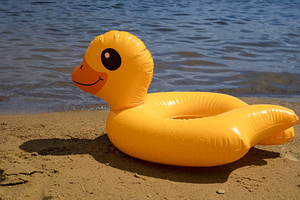 istock Bright yellow inflatable duck float resting on sandy beach by water 2219754632