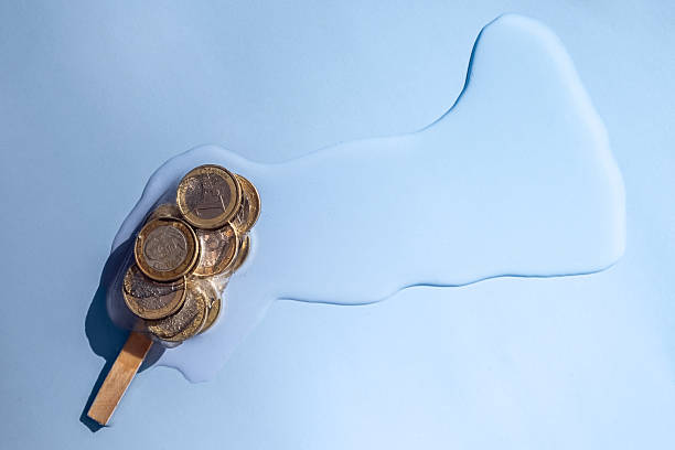 Creative conceptual image of euro coins frozen inside a popsicle against a blue background, symbolizing economy, finance, or inflation.