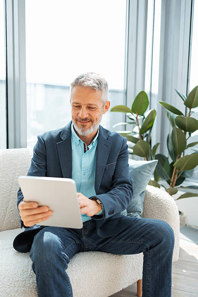 istock Smiling man uses a tablet while sitting comfortably in a bright modern room. 2219757231