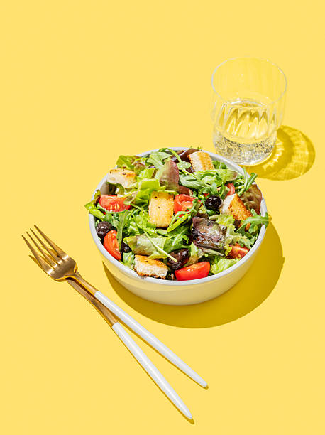 Vegetable salad with lettuce, tomatoes, croutons and olives in a bowl on a yellow background