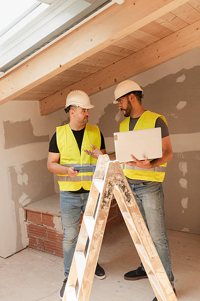 istock Two male Construction workers in safety vests using laptop discussing renovation project indoors 2219763490