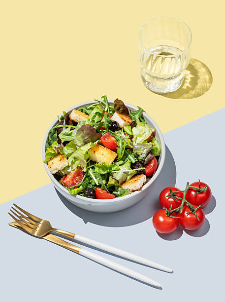 Salad with lettuce, tomatoes, croutons and olives in a bowl on a yellow blue background
