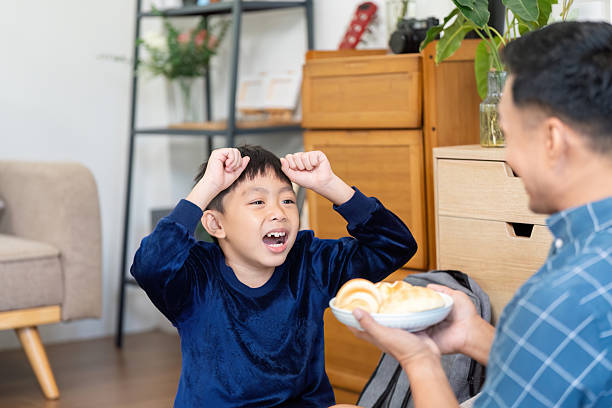 istock Joyful Child Celebrating with Snacks. A young boy expresses excitement while receiving treats from his father. 2219768730