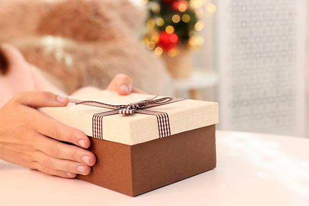istock Woman holding Christmas gift box with makeup brushes and cosmetics at white table, closeup 2219770046
