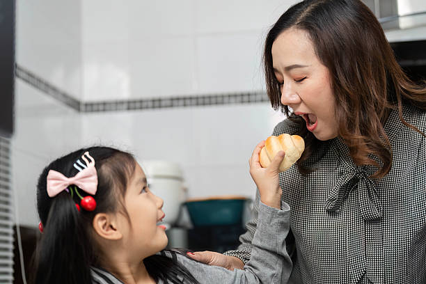 istock Playful Eating Moment. Child playfully feeding mother with pastry in bright kitchen. 2219771608