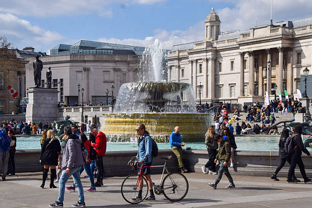 London, United Kingdom - Apr 19, 2019 : Busy afternoon at Trafalgar square. Locals and tourists visiting sit by fountain in Trafalgar Square. Trafalgar Square is a public space and tourist attraction in central London. Selective focus.