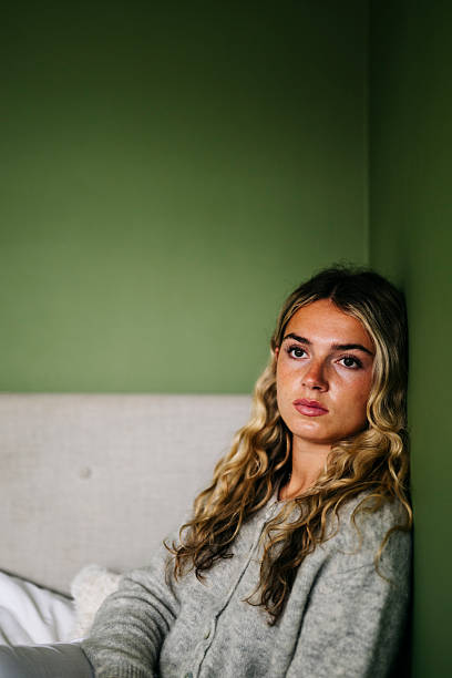 Young woman sitting alone in her bedroom looking thoughtful