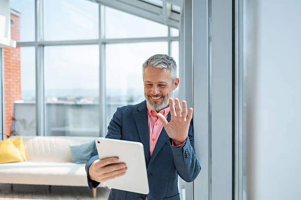 istock Mature businessman waving during a video call on a tablet in a bright office 2219778013