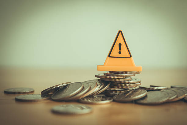 istock Yellow warning sign label on stack coins crash on wooden table with white background copy space. 2219778479