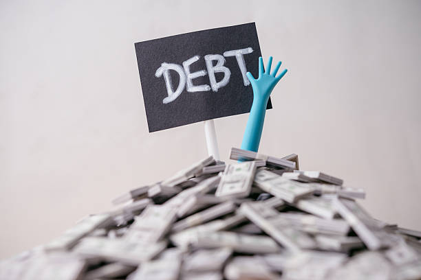 istock Pop out hand from heap US dollar banknotes and DEBT label white wall background. 2219778510
