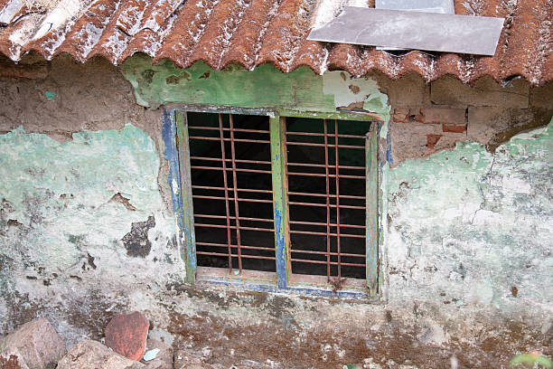 Old house in Munnar, India, aged rustic window grilles, facade with broken green colored wall, brick and stone building