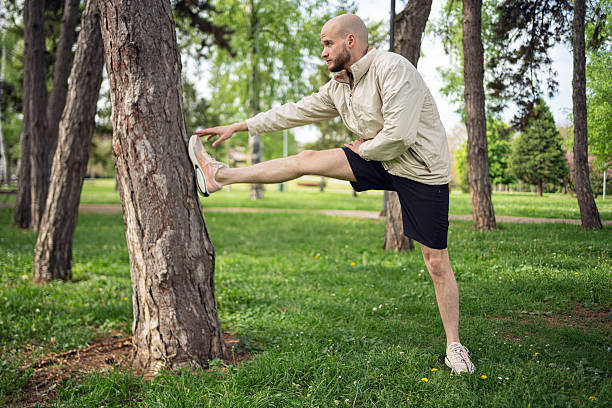 istock Bald man stretching leg on tree in park during fitness exercise 2219783825