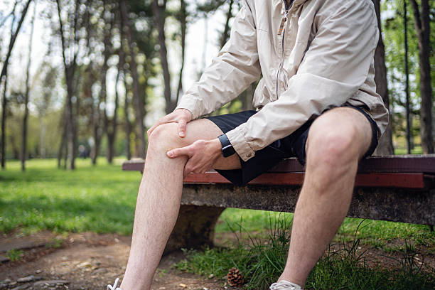 istock Man sitting on a park bench holding his knee with visible distress 2219783843