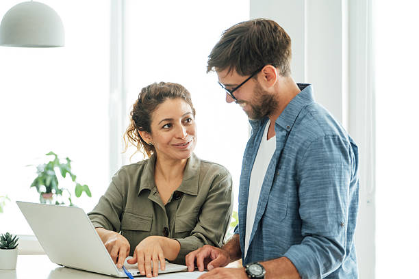 istock Two colleagues engage in a collaborative discussion at an office desk with a laptop and documents in a bright modern workspace 2219784129