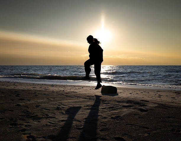 Cropped shot of the legs of youthful friends playing with ball together on the beach at sunset on a golden summer evening. Couple walking barefoot on sandy beach. They are walking, having fun.