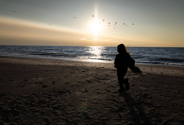 A girl plays and runs on the beach while being backlit by the setting sun