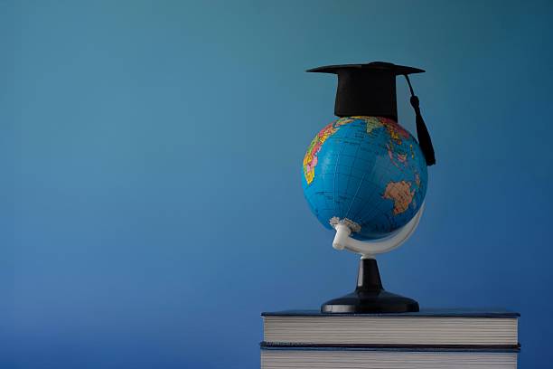istock A globe wearing a black graduation cap on a stack of books against a solid blue background. 2219785321