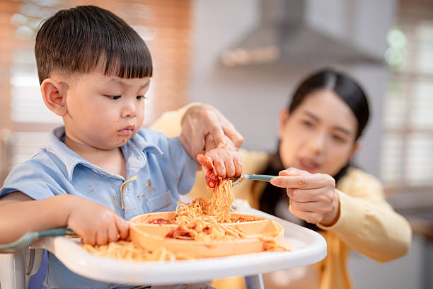 istock Messy mealtime experience with a young boy eating spaghetti and a mother helping in a bright kitchen 2219790852