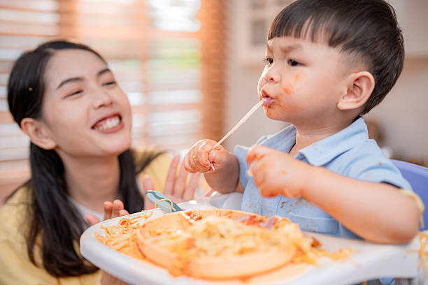 istock Toddler enjoys spaghetti while caregiver playfully engages in a kitchen setting during late afternoon family meal 2219790883