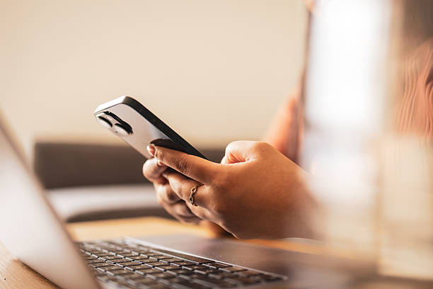 istock Person using smartphone while working on a laptop at a desk 2219792927
