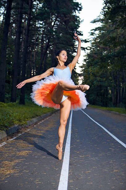 istock Flexible Slim Young Caucasian Ballet Dancer in Light Orange Blue Tutu Posing in Dance Pose During Ballet Pas in Summer Forest With Lifted Hands 2219794709