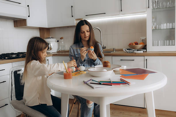 istock Two Girls Decorating Easter Eggs Together in a Home Kitchen 2219798710