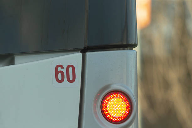 This detailed image shows a closeup of a city buss rear end, featuring the bold numeral 60 and a bright red warning light, highlighting key aspects of urban transportation