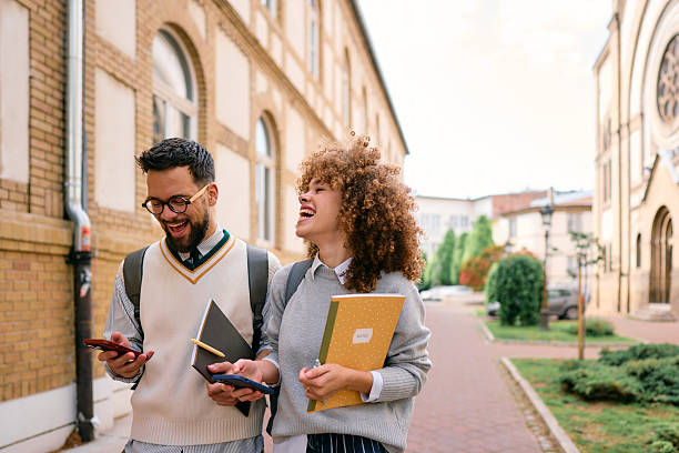 istock Cheerful students laughing and using smartphones while walking near university building 2219800863