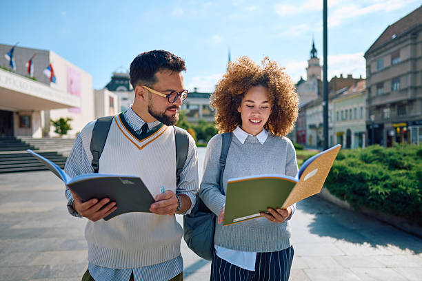 Two Smiling Students Reading Books While Walking in a City