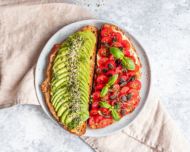 Close-up of a pair of organic hass avocados hanging from the branch of a tree in cultivation on a blurred background - Stock Photo