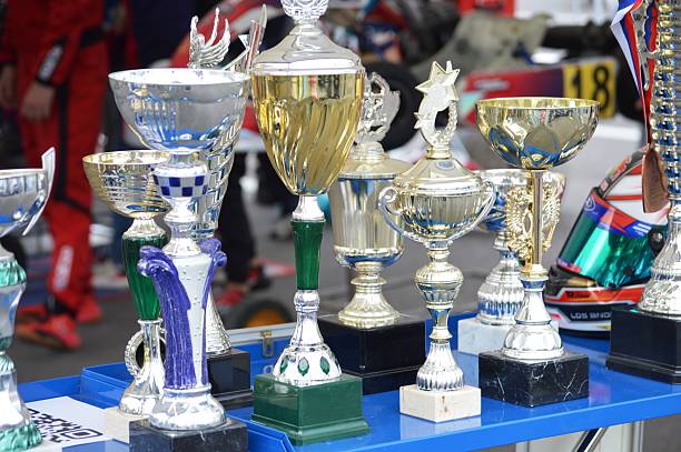 Close-Up Of Coins Stack With Toy Blocks By Trophy On Table Against Red Background